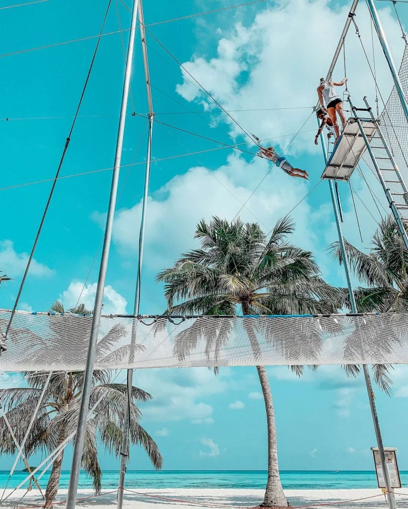 Flying trapeze rig with flyer mid-swing over the beach — Club Med Kani, Maldives — MACA flying trapeze rig