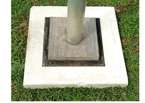 Concrete pole base with wooden base under a rig pole, installed on grass — MACA flying trapeze rig