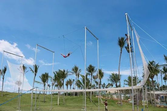 Flyer mid-air on a flying trapeze rig against blue sky and palms — Shangri-La Hambantota, Sri Lanka — MACA flying trapeze rig
